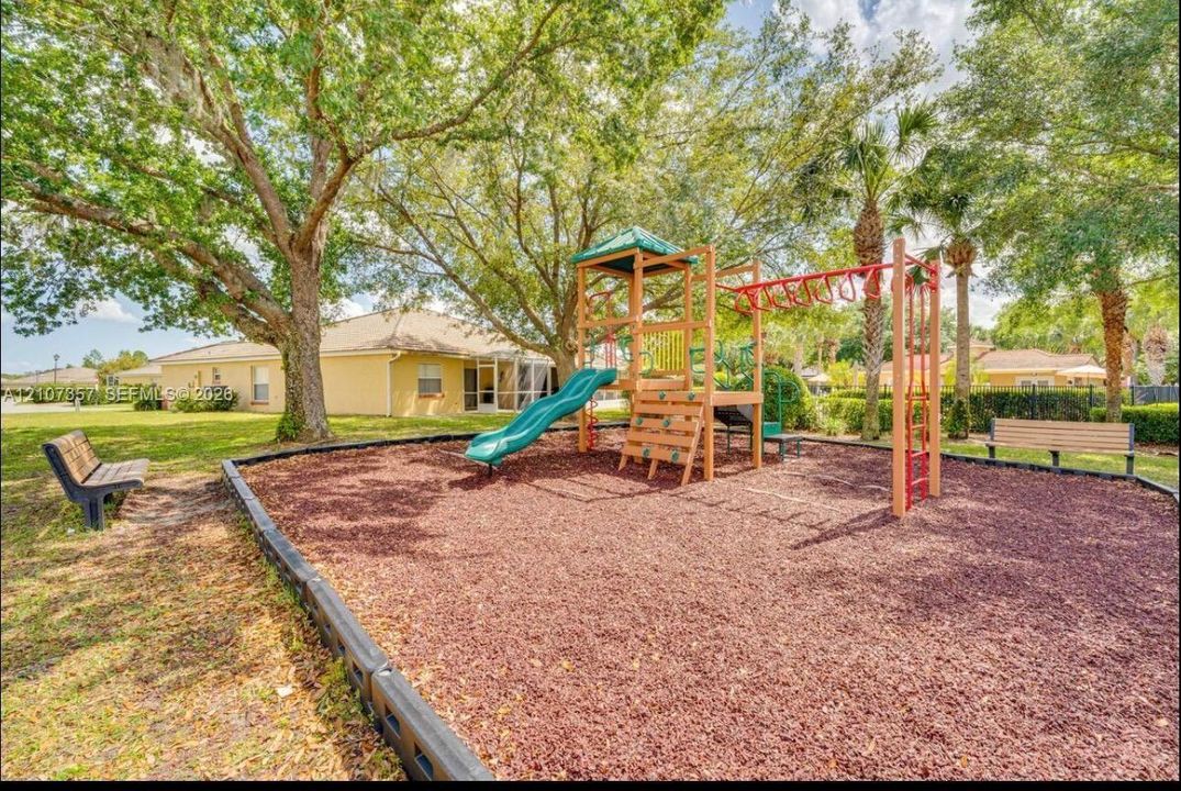 Recreational area featuring a playground structure with a slide and climbing wall, rubberized ground cover, and surrounding mature trees