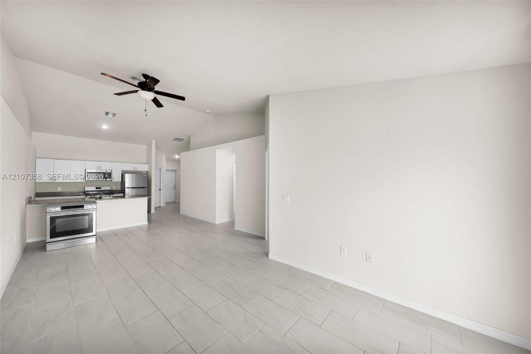 Vaulted ceilings, large-format tile flooring, kitchen featuring stainless steel appliances, white cabinetry, and ceiling fan