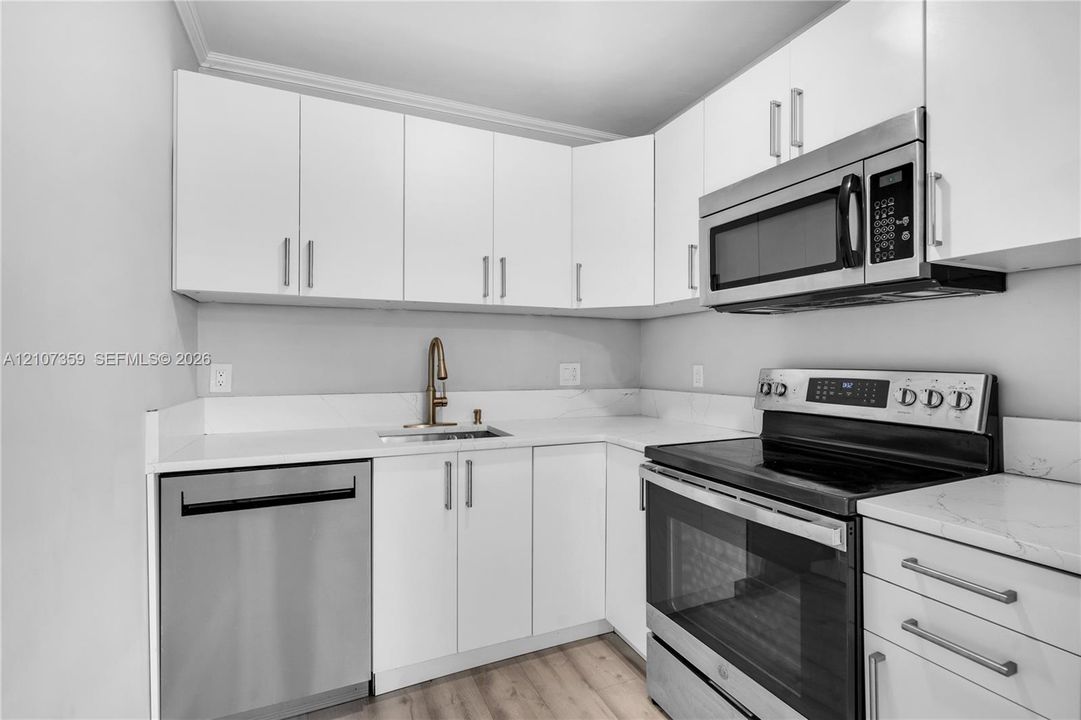 Kitchen featuring white shaker-style cabinetry, solid-surface countertops, and stainless steel appliances including an over-the-range microwave