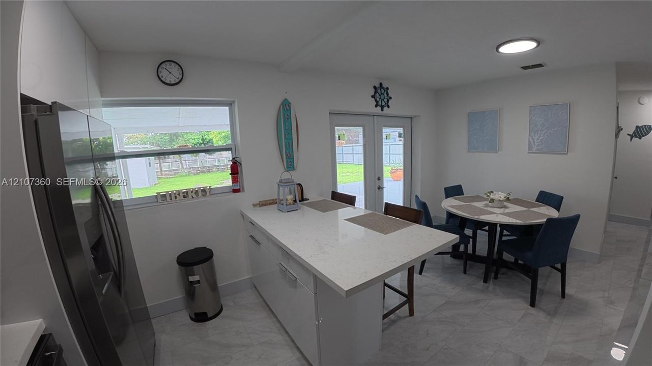 Kitchen featuring an island with a stone-surface countertop, white cabinetry, tile flooring, stainless steel refrigerator, and glass-paneled double doors
