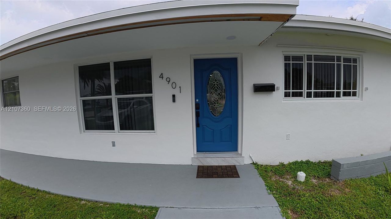Exterior entrance featuring a painted white facade, blue front door with decorative glass insert, multi-pane windows, and a paved covered porch