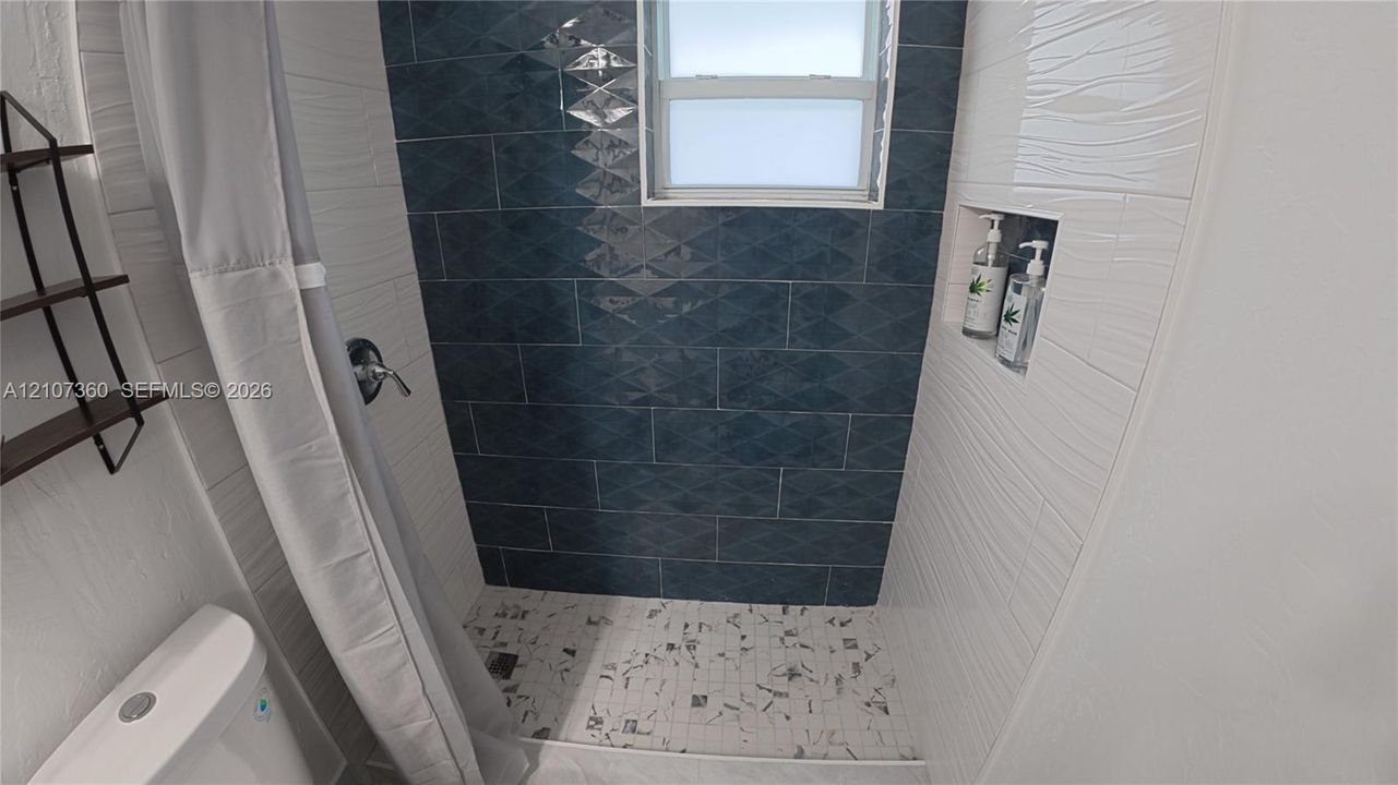 Shower area featuring blue geometric-patterned wall tiles, white textured wall tiles, a built-in recessed niche, and mosaic floor tile