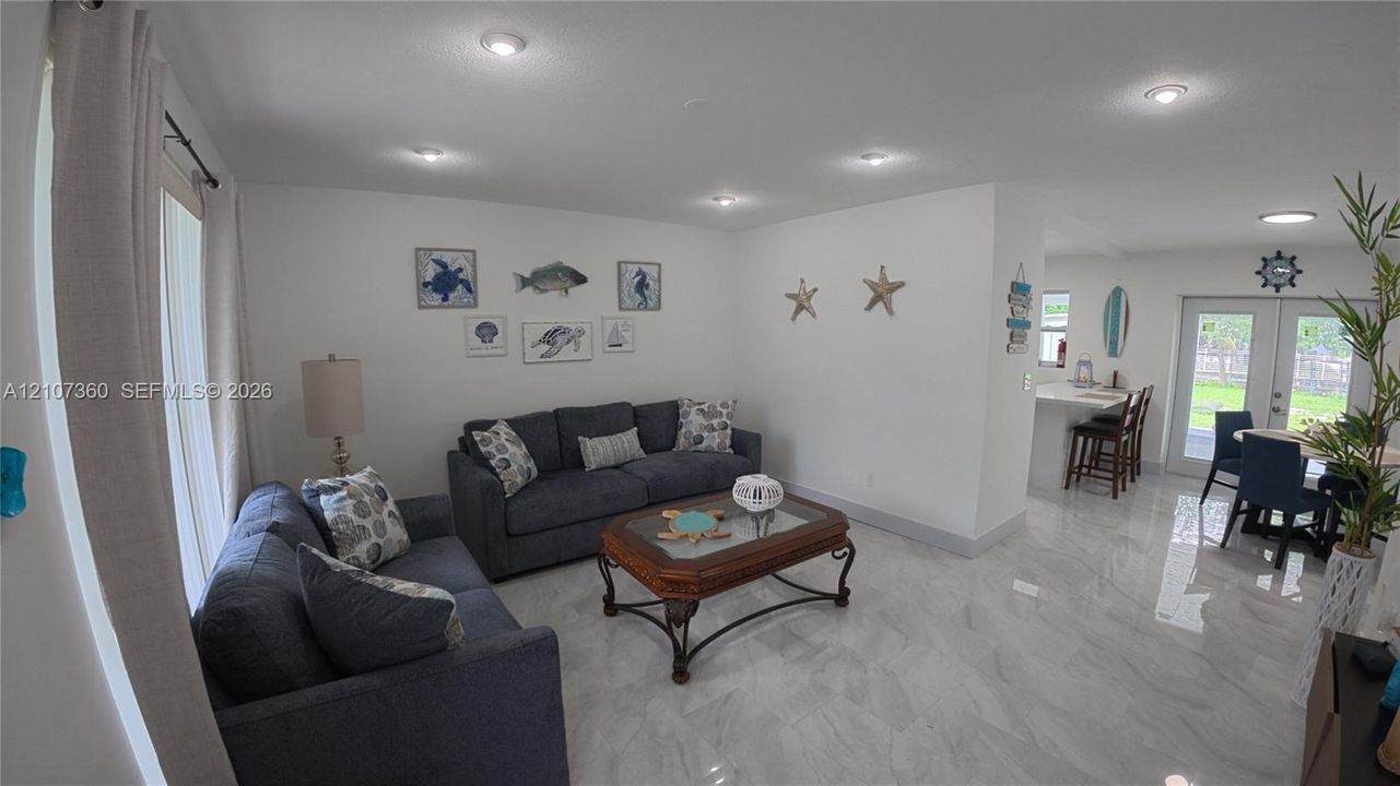 Open-concept interior featuring light-toned tile flooring, recessed ceiling lighting, and double-door access to the exterior
