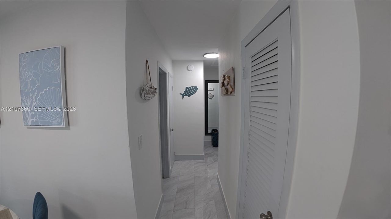 Neutral-toned interior hallway featuring stone-finish tile flooring, a louvered-panel closet door, and a flush-mount circular ceiling light fixture