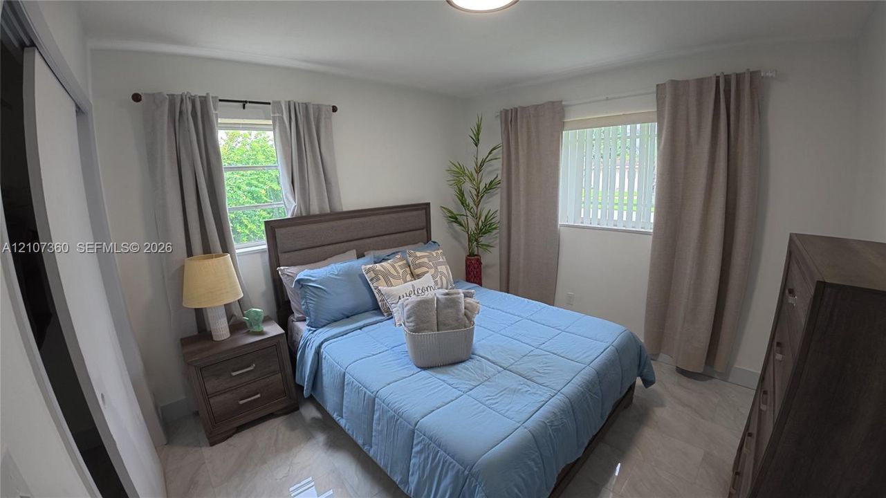 Neutral-toned interior featuring large-format tile flooring, dual windows with blinds, and sliding closet doors