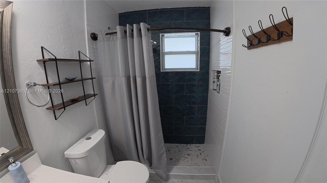 Bathroom featuring a tiled shower surround with recessed shelving, a curved shower rod, and a multi-purpose wall-mounted rack