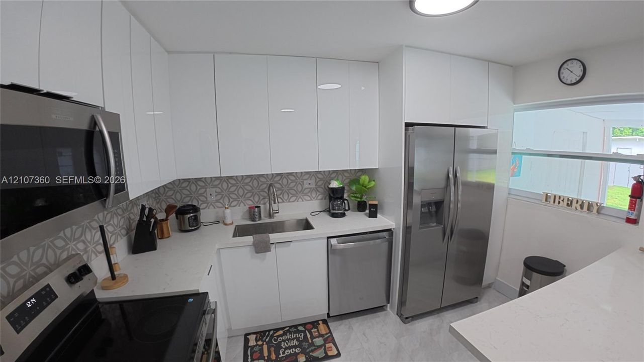 Kitchen featuring white flat-panel cabinetry, light-toned stone countertops, stainless steel appliances, and a geometric-patterned tile backsplash