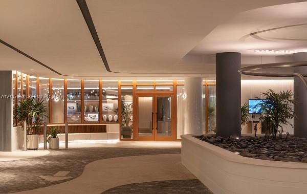 Contemporary lobby featuring recessed ceiling lighting, a wood-framed glass entryway, integrated wall shelving, a stone-filled planter, and decorative support columns
