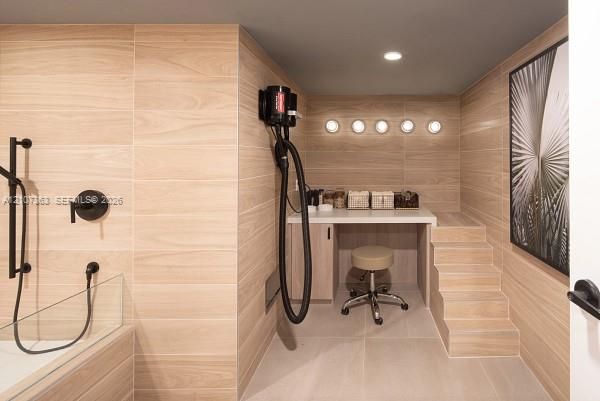 Floor-to-ceiling light wood-finish wall paneling, built-in vanity with quartz countertop, integrated five-light recessed fixture, stepped platform, and matte black shower hardware