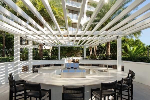 Outdoor entertainment area featuring a circular stone countertop with an integrated stainless steel grill and sink, sheltered by a white pergola structure and enclosed by curved masonry walls