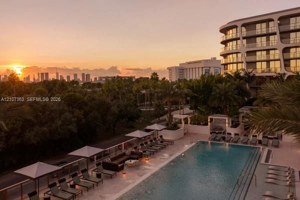Swimming pool with stone decking, integrated sun shelf, and perimeter landscaping, featuring an architectural multi-story exterior with floor-to-ceiling glass and geometric facade detailing