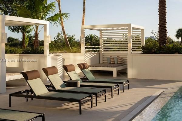 Outdoor lounge area featuring a tiled pool deck, built-in masonry planters, and wood-slat privacy cabanas with wall-mounted lighting