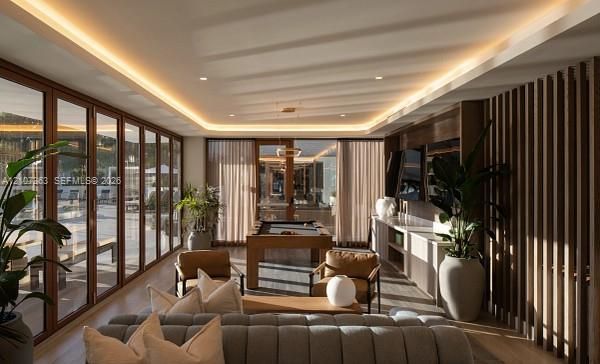 Floor-to-ceiling glass wall panels, recessed cove lighting, built-in cabinetry with integrated shelving, and vertical wood-slat wall paneling