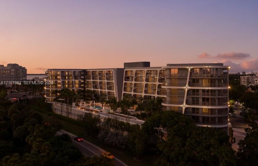 Multi-story contemporary residential building featuring a distinctive geometric facade, private balconies, an elevated swimming pool, and lush landscaping