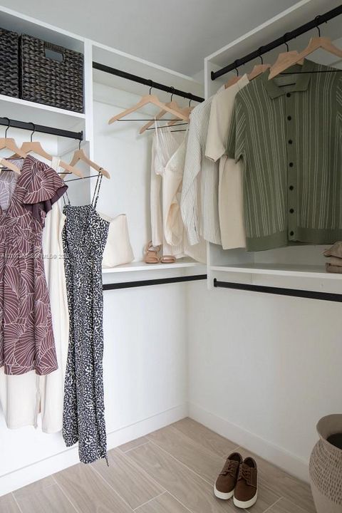 Customized walk-in closet featuring floor-to-ceiling white cabinetry, integrated shelving units, and matte black hanging rods