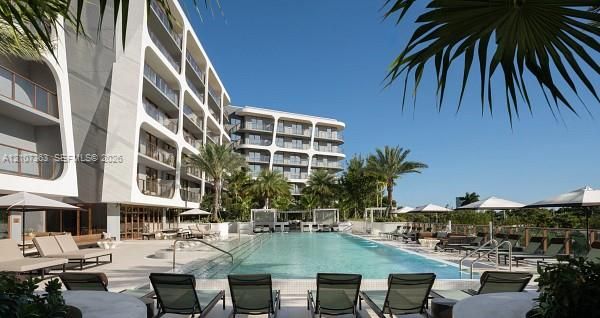 Multi-story modern building featuring recessed private balconies, a rectangular swimming pool, integrated hardscaping, and mature palm trees