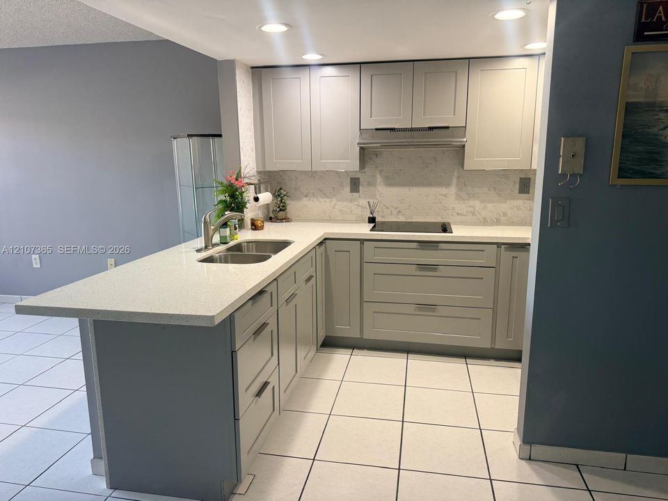 Kitchen featuring light gray shaker-style cabinetry, quartz countertops, a dual-basin stainless steel sink, a smooth-top electric cooktop, and tile flooring