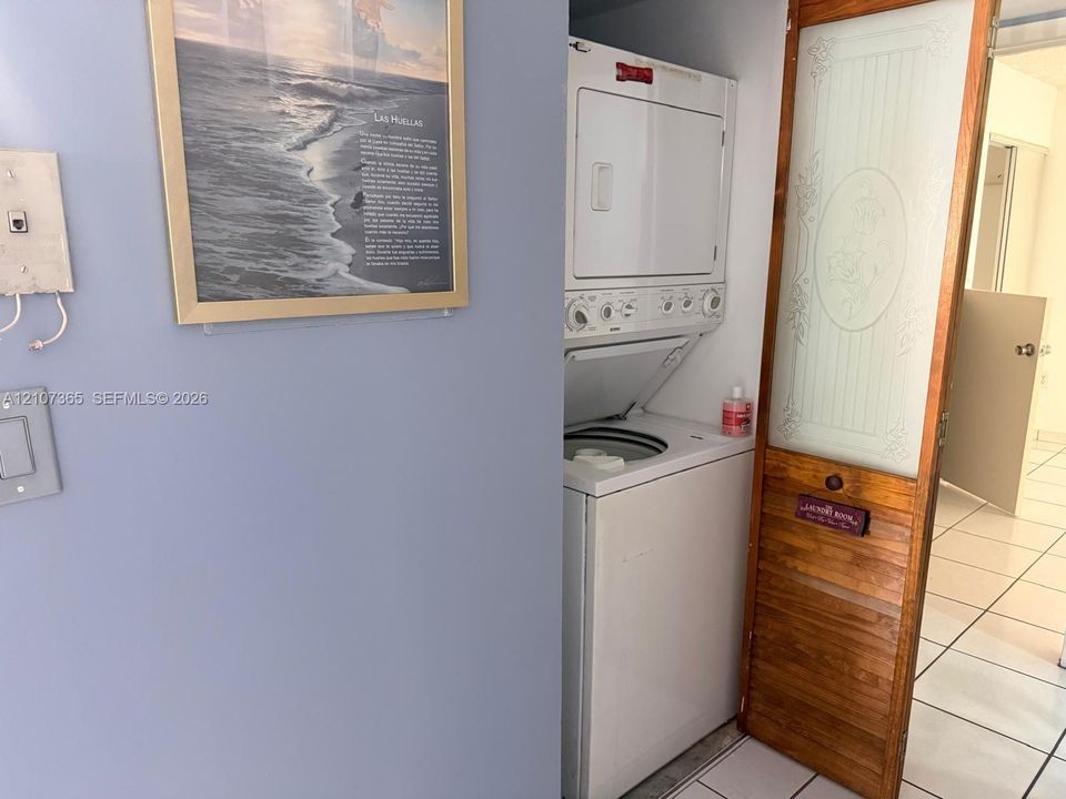Stacked laundry unit featuring a white finish, enclosed by a wood-framed door with a frosted glass panel and decorative etching, set against tile flooring