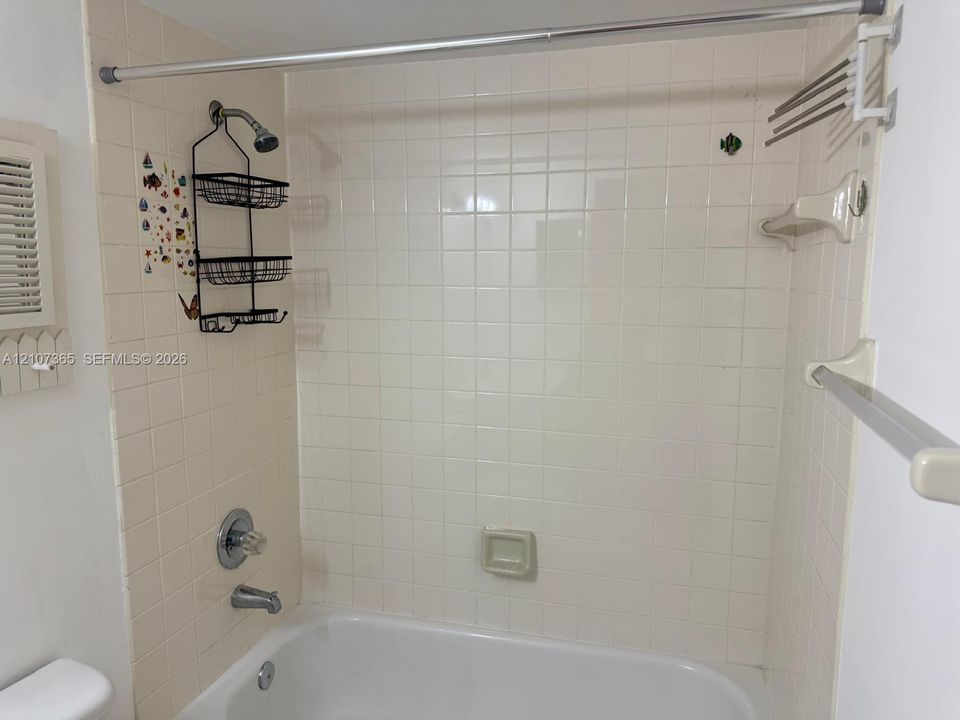 Shower and bathtub combination featuring white square wall tiling, chrome fixtures, a recessed soap dish, and a metal tension shower rod