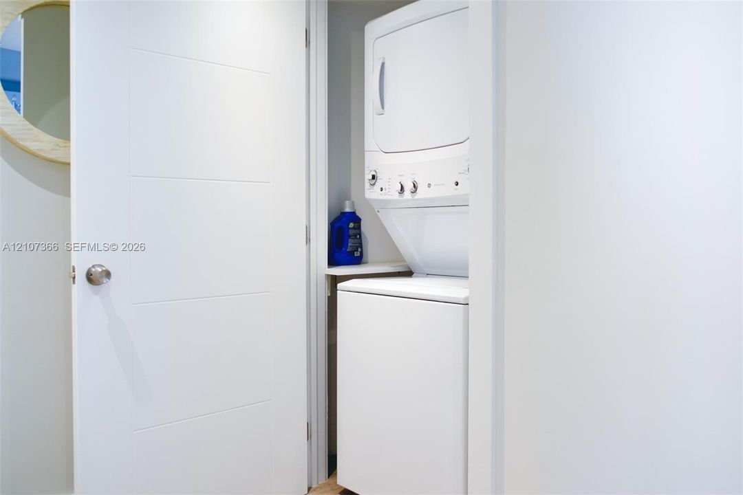 Stacked laundry unit featuring a white appliance finish and a built-in shelving ledge