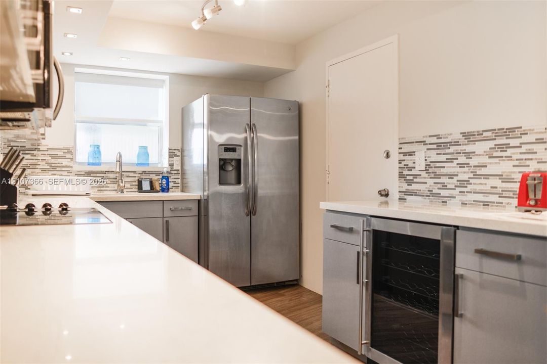 Kitchen featuring white countertops, grey flat-panel cabinetry, a stainless steel side-by-side refrigerator, a built-in stainless steel beverage cooler, and horizontal mosaic tile backsplashes