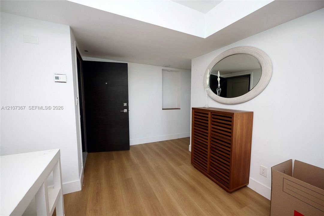 Entryway featuring wood-finish flooring, a dark-finish solid core door with a matte metallic handle, and a built-in recessed niche
