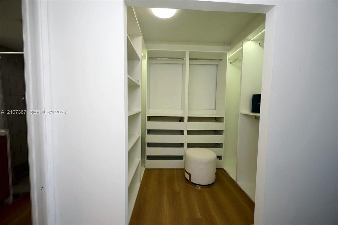 Walk-in closet featuring white built-in shelving, integrated dresser drawers, hanging rods, recessed ceiling lighting, and wood-finish flooring