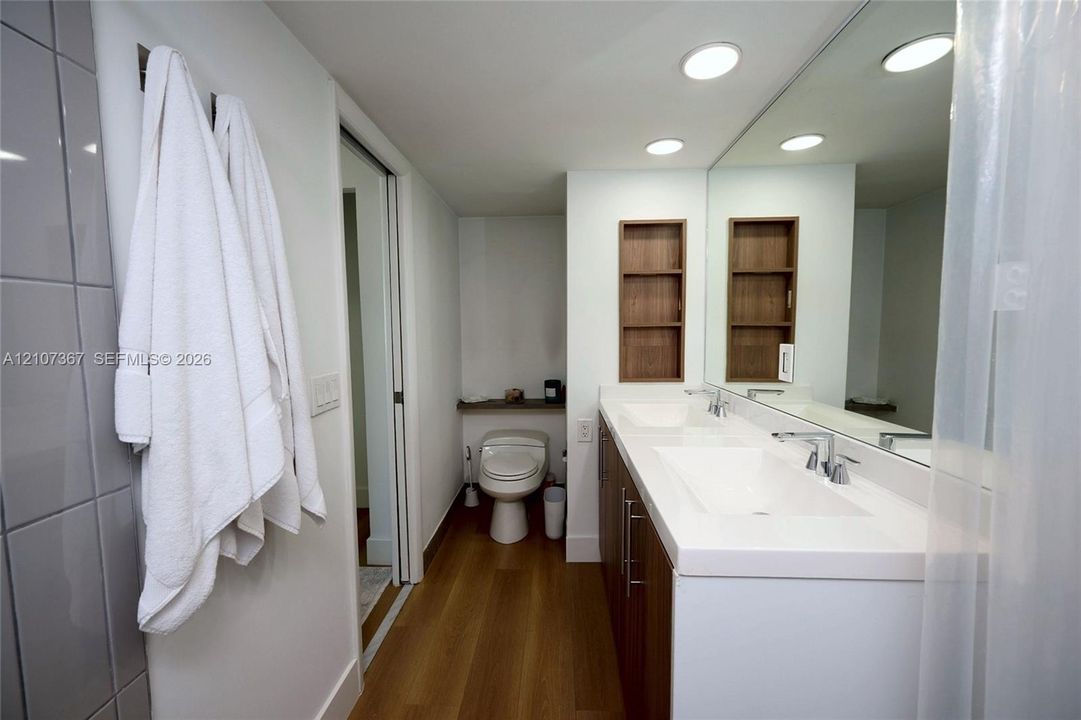 Double vanity featuring white integrated sinks, wood-finish cabinetry, recessed lighting, and wall-recessed shelving