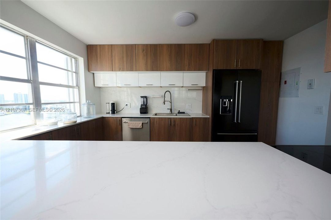 Kitchen featuring white solid-surface countertops, two-tone wood-finish and high-gloss white cabinetry, stainless steel appliances, and a high-arch pull-down faucet