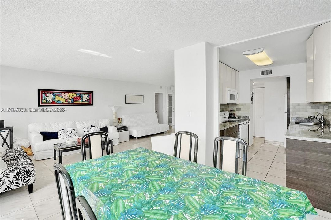 Open-concept interior featuring large-format tile flooring, a kitchen equipped with two-tone cabinetry, stone-finish countertops, and an undermount stainless steel sink