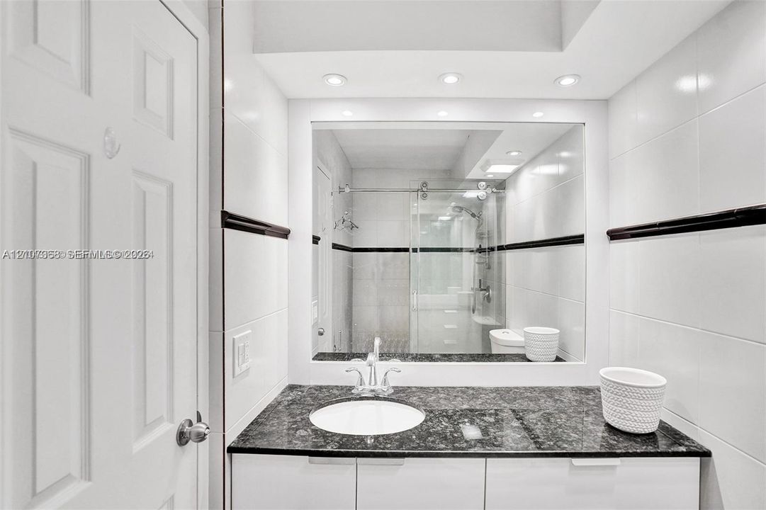 Bathroom featuring a stone-surface vanity with an integrated basin, high-gloss white cabinetry, large-format wall tiling with a dark decorative accent border, and a glass-enclosed shower stall with sliding hardware