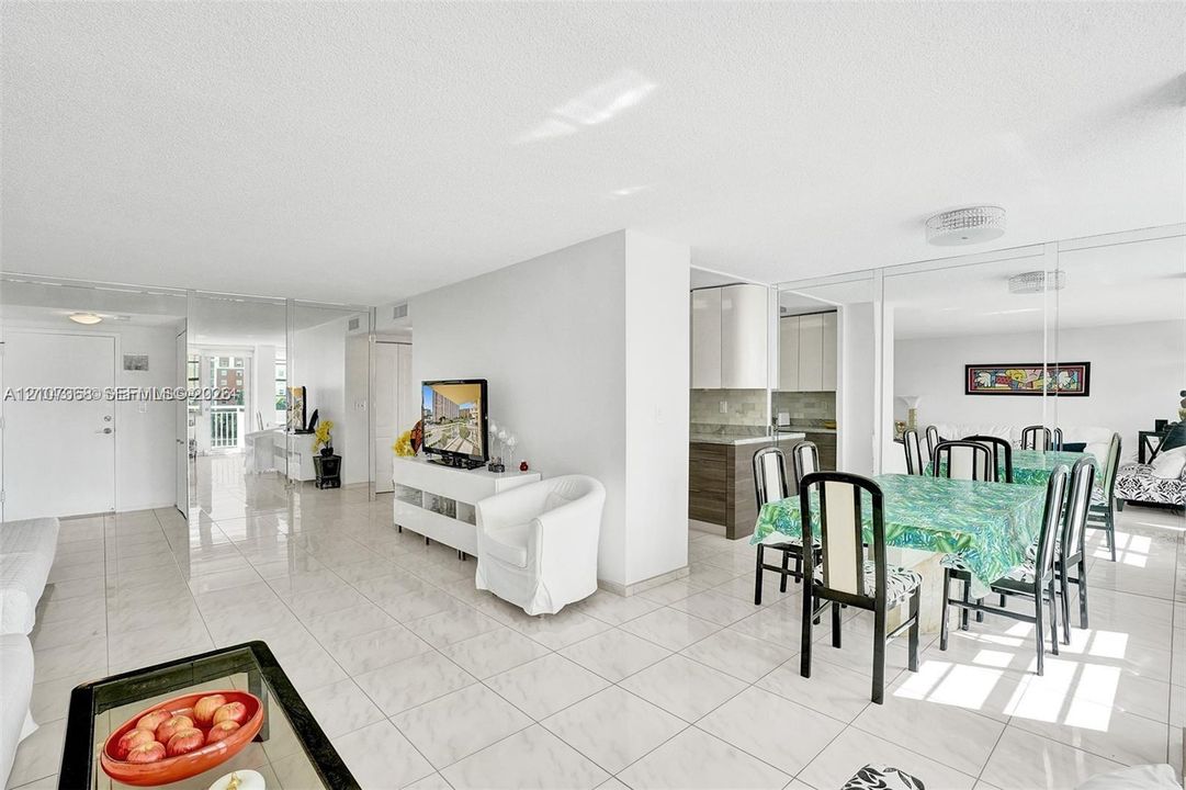 Open-concept floor plan featuring light-toned tile flooring, floor-to-ceiling mirror paneling, and a kitchen equipped with cabinetry and stone-surface counters