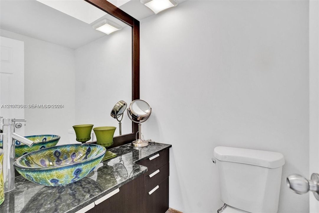 Dark-finish vanity cabinetry with a stone countertop, glass vessel sink, polished chrome faucet, and large-format framed mirror