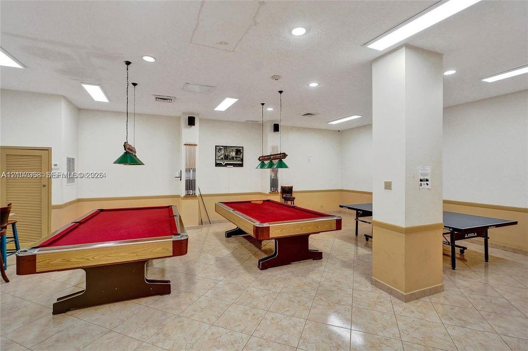 Large recreation room featuring tile flooring, neutral wall coloring with wainscoting, recessed lighting, and dual billiard light fixtures
