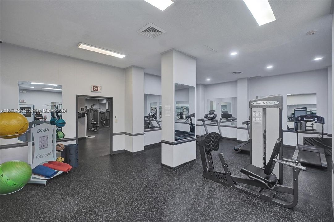 Fitness room featuring rubberized flooring, recessed ceiling lighting, wall-to-wall mirrors, and structural columns