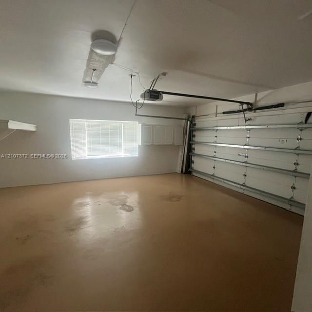 Garage space featuring an epoxy-coated floor, horizontal window with blinds, overhead light fixtures, and wall-mounted cabinetry