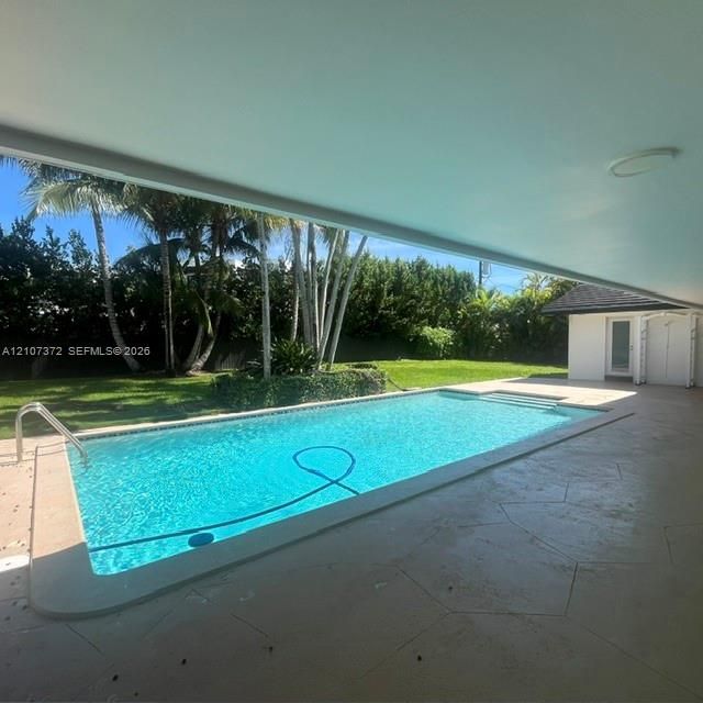 In-ground swimming pool with built-in stairs, expansive concrete patio, and manicured lawn