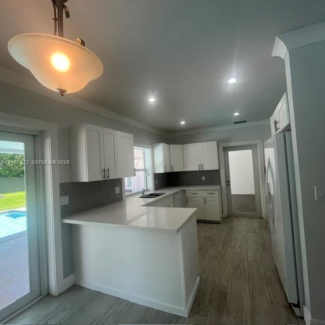 Kitchen featuring white shaker-style cabinetry, solid-surface countertops, wood-finish flooring, recessed lighting, and a glass-paneled exterior door