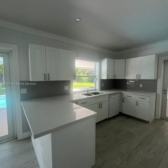 Kitchen featuring white shaker-style cabinetry, solid-surface countertops, grey subway tile backsplash, stainless steel dual-basin sink, and wood-finish tile flooring