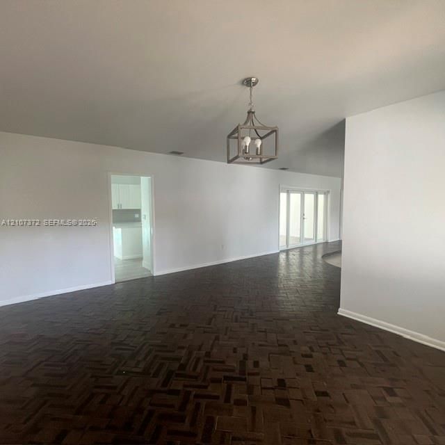 Herringbone-patterned wood flooring, open-concept interior, multi-pane glass exterior doors, and a geometric metal cage chandelier