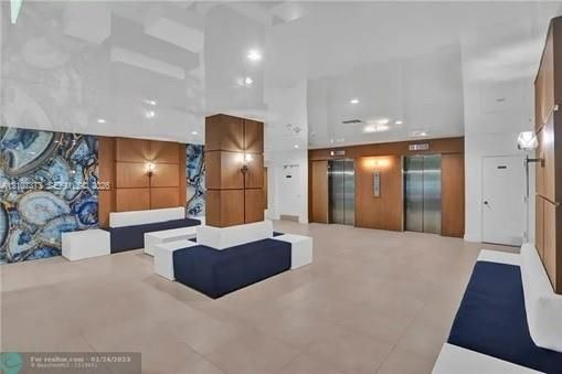 Lobby featuring high-gloss ceiling, stone-accented walls, wood-paneled columns, built-in seating, and metallic elevator doors