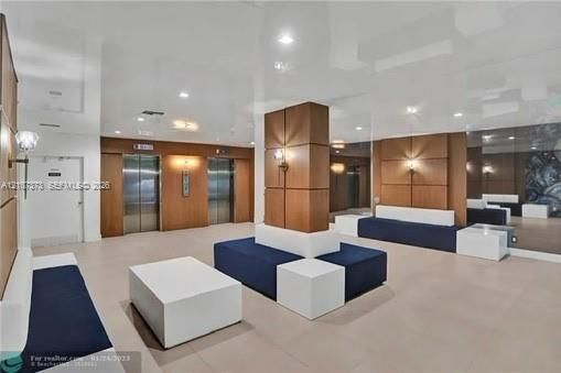 Lobby area featuring high-gloss reflective ceilings, wood-panel wall accents, recessed lighting, dual elevator access, and floor-to-ceiling mirror panels