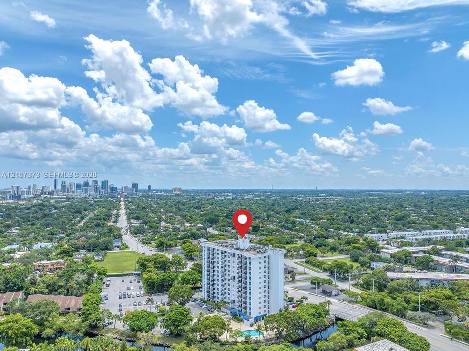 High-rise building featuring a white facade, a dedicated surface parking lot, an on-site swimming pool, and mature tree-lined surroundings