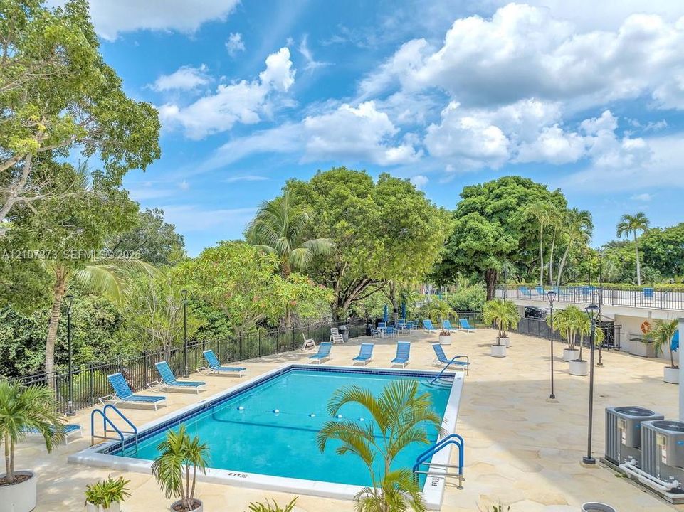 In-ground swimming pool featuring a flagstone deck, metal safety fencing, built-in handrails, and mature landscaping