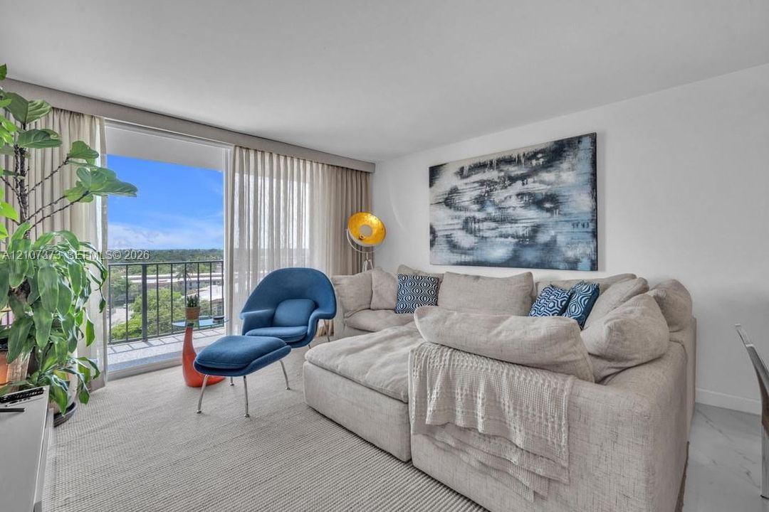 Sliding glass door opening to a private balcony with metal railing, floor-to-ceiling drapery, and large-format tile flooring