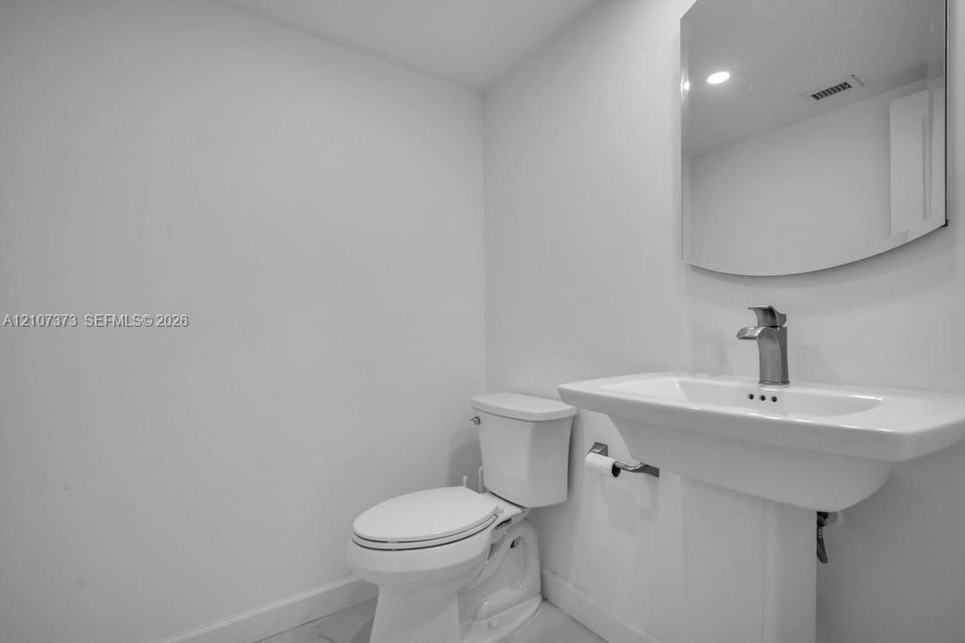 Half Bathroom Pedestal sink featuring a polished chrome faucet, wall-mounted mirror, and white ceramic toilet