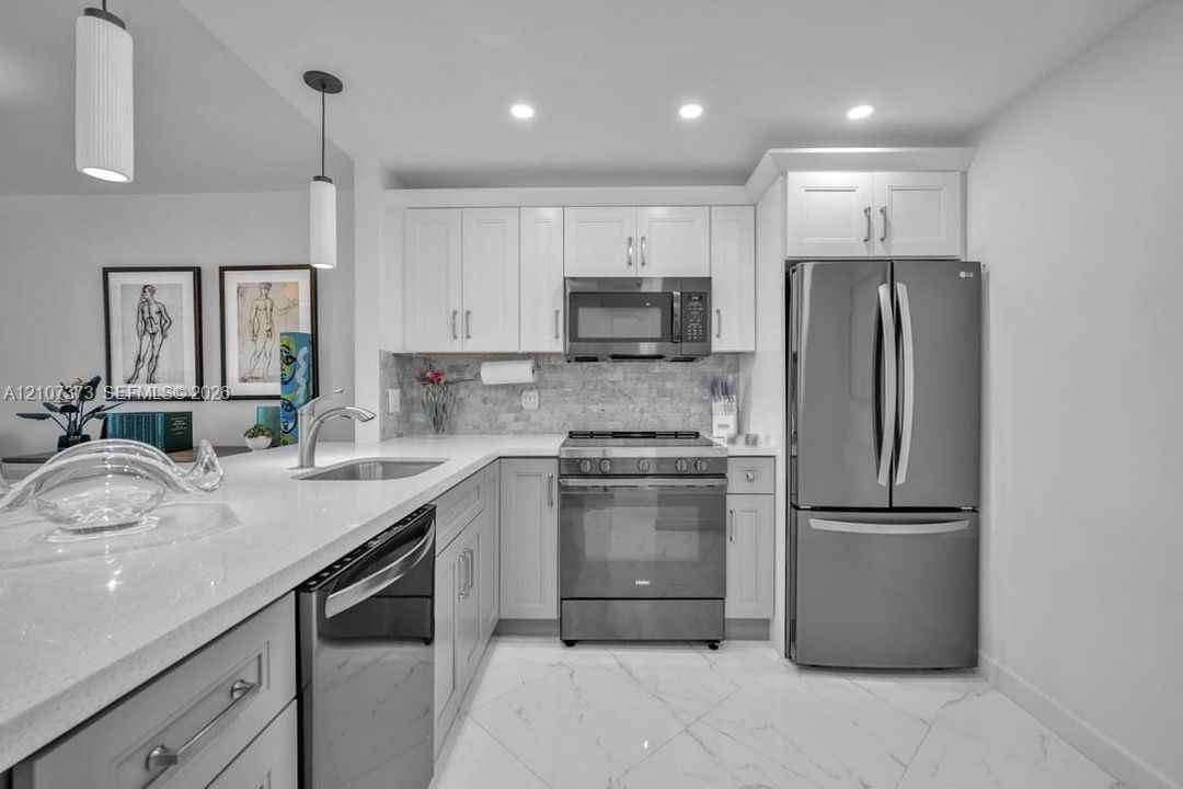 Kitchen featuring white cabinetry, solid-surface countertops, stone tile backsplash, stainless steel appliances, and large-format tile flooring