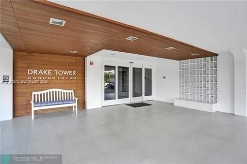Covered entryway featuring wood-finish ceiling paneling, large-format tile flooring, recessed lighting, and decorative architectural screen wall