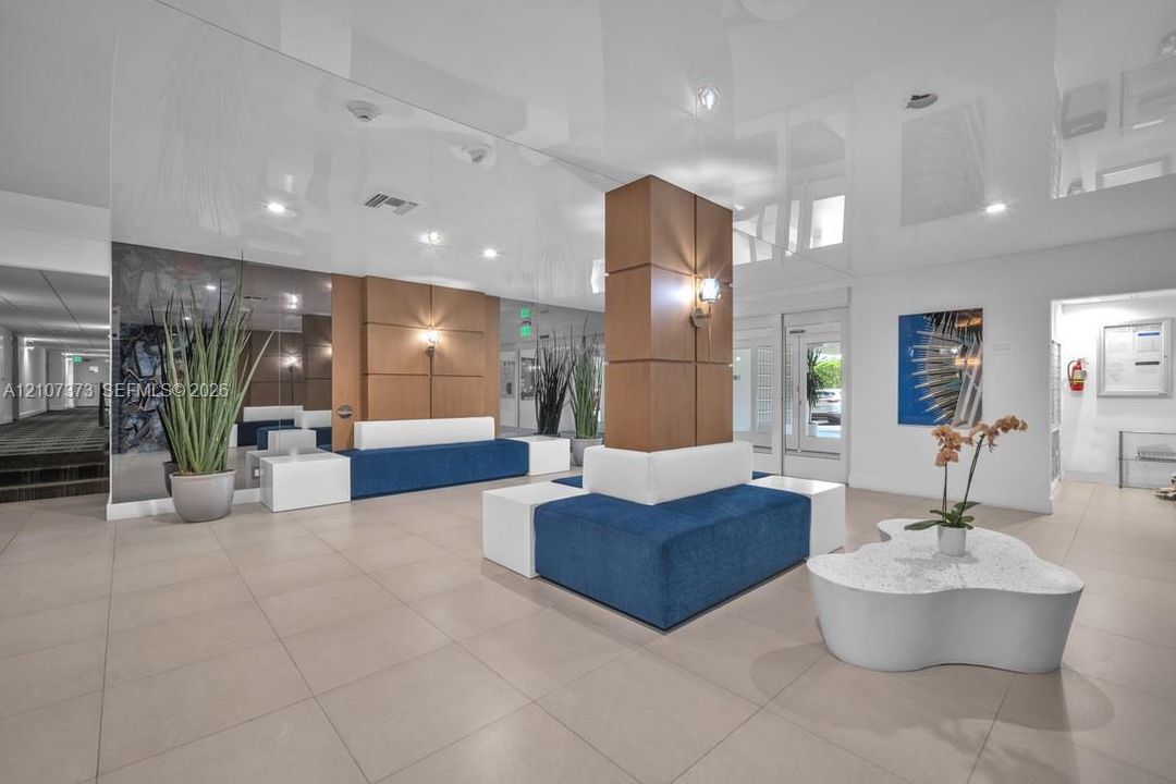 Lobby featuring high-gloss ceilings, large-format tile flooring, mirrored wall accents, and wood-paneled structural columns with integrated sconce lighting