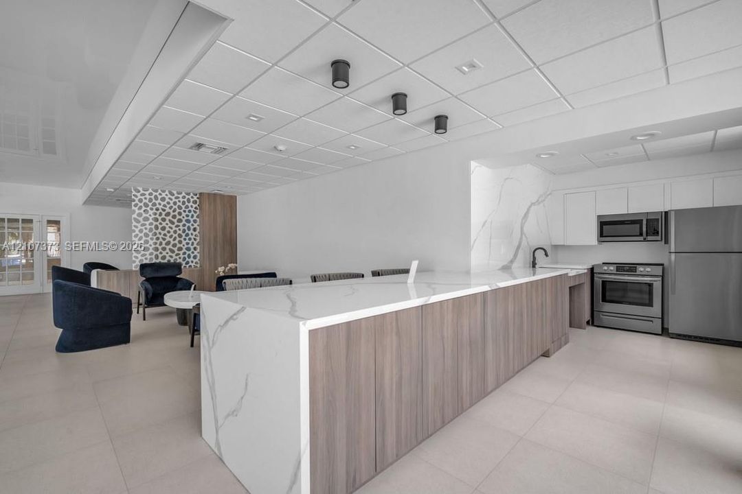 Large kitchen island featuring waterfall-edge composite stone countertops and wood-finish cabinetry, accented by stone slab backsplashes and stainless steel appliances